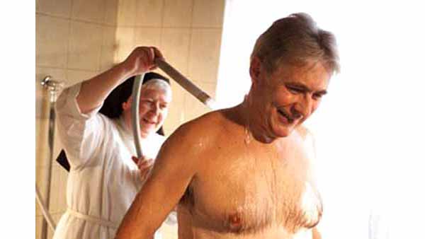 A shirtless man receiving a shower from a smiling nun